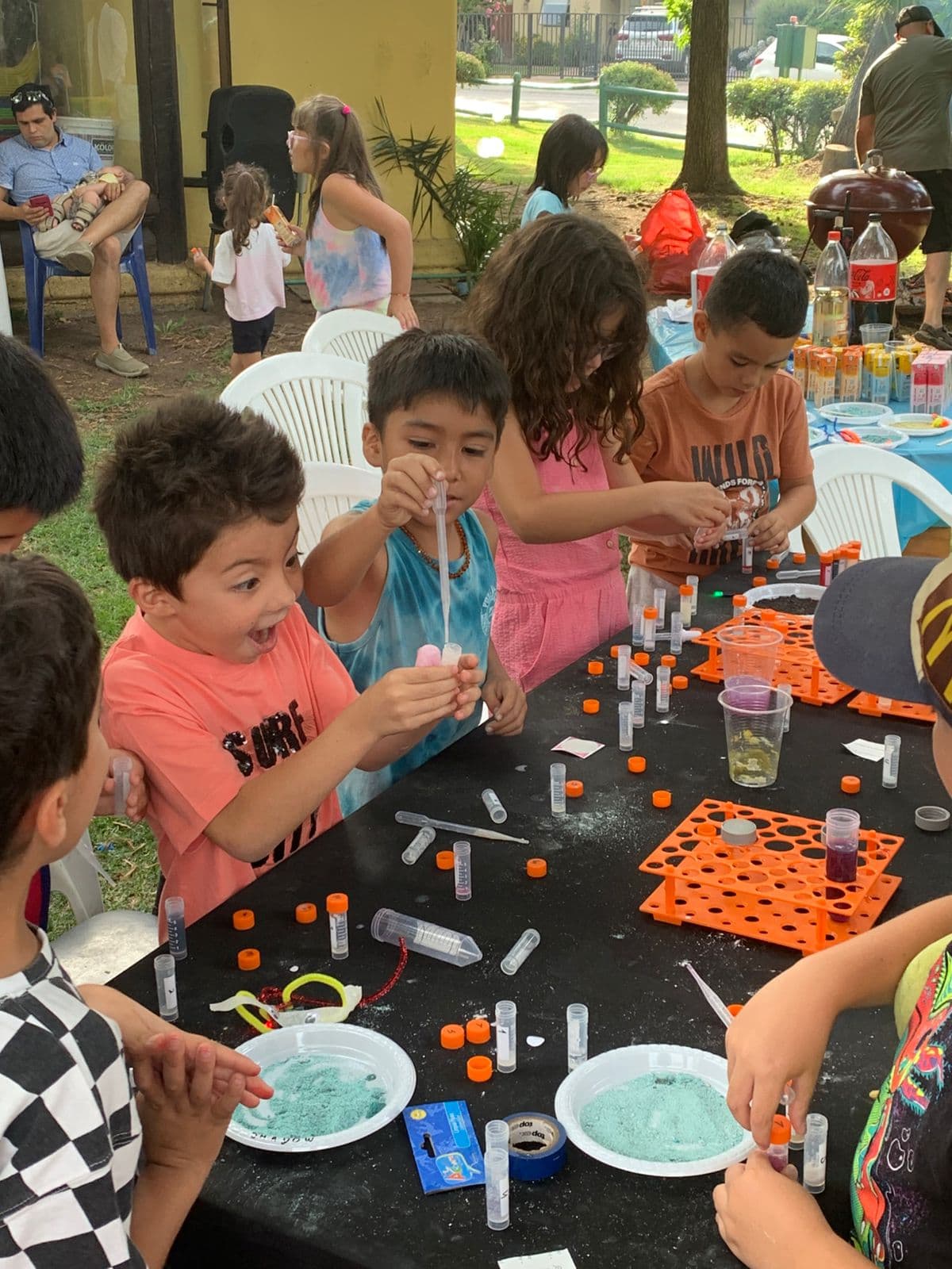 Niños experimentando con pipetas y tubos de ensayo en una mesa, uno de ellos con expresión de sorpresa
